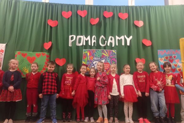 uczniowie ubrani na czerwono przy napisie POMAGAMY