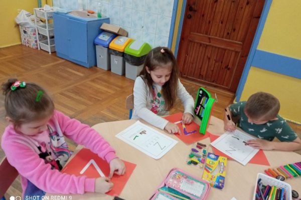 Dzieci siedzą przy stolikach wyklejają plasteliną literę z