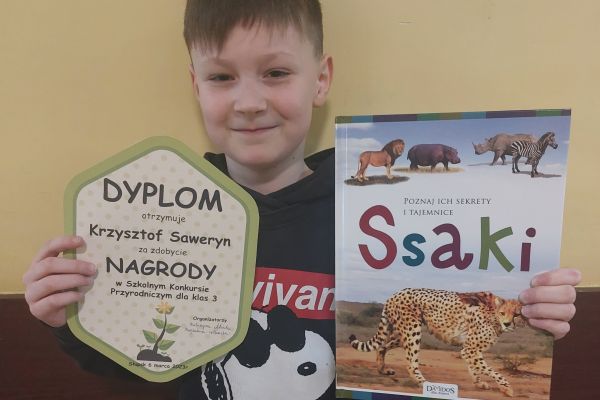 Laureat Szkolnego Konkursu Przyrodniczego pozuje z dyplomem i nagrodą.